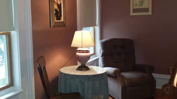 A room with a round table, a chair, a lamp, and a cushioned armchair.