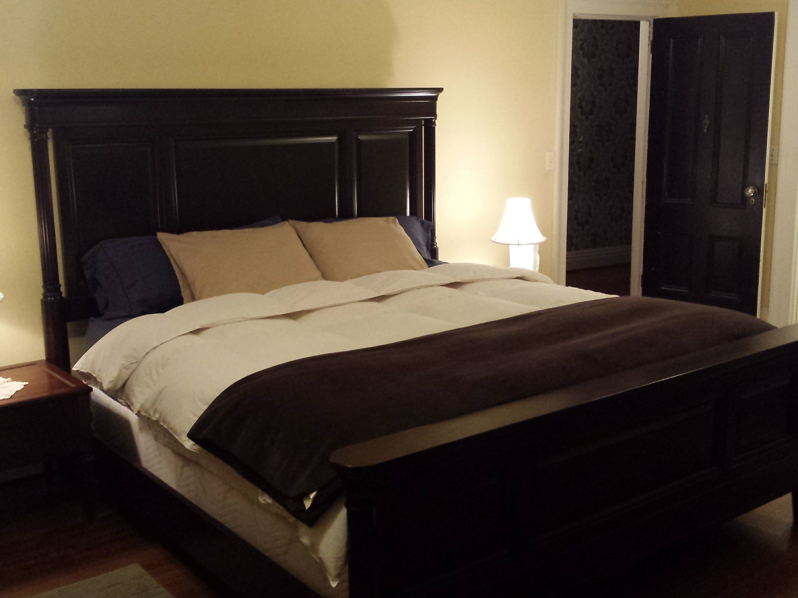 Un lit bien fait, avec une tête de lit sombre, une lampe de chevet et une porte ornée d’un motif décoratif.