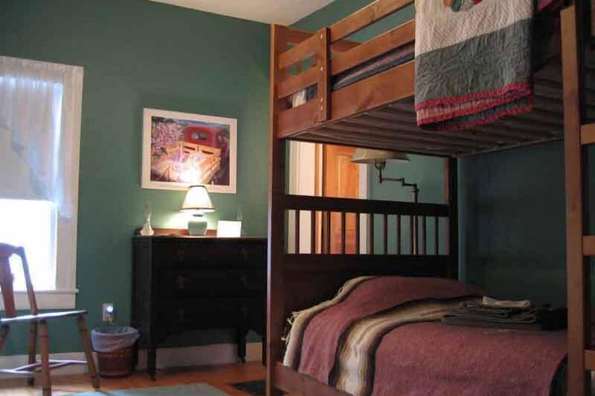 A bunk bed room with a desk, chair, and a painting on the wall.