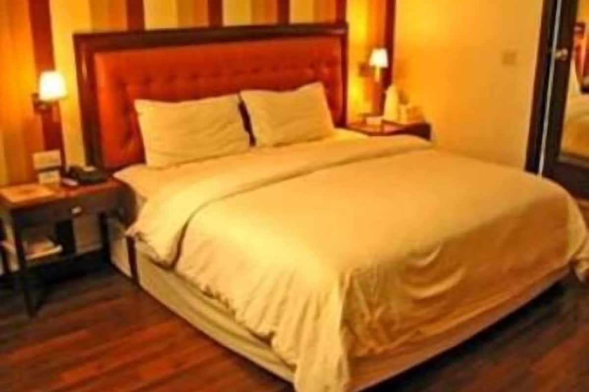 A neatly made bed with a wooden headboard, a bedside table with a lamp, and a nightstand with a lamp.
