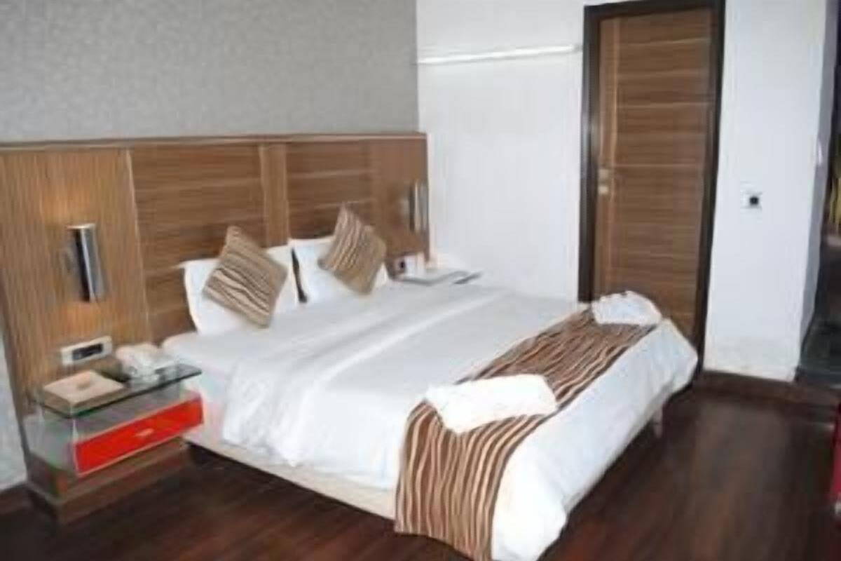 A hotel room with a wooden headboard, a bed with white bedding, a bedside table with a glass top, and a red drawer.