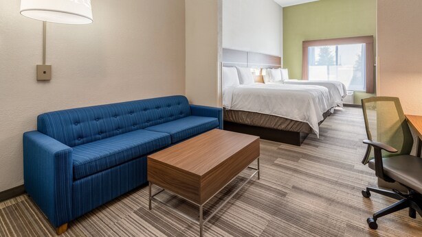 A hotel room with a blue sofa, a wooden coffee table, a bed with white bedding, and a chair.