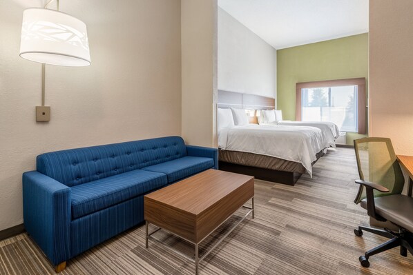 A hotel room with a blue sofa, a wooden coffee table, a bed with white bedding, and a chair.
