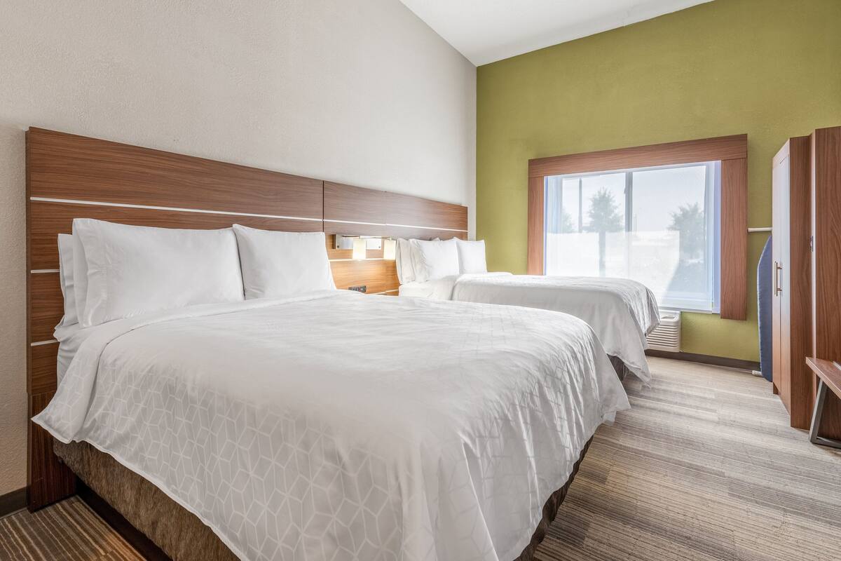 A hotel room with two beds, a large window, and a wooden headboard.