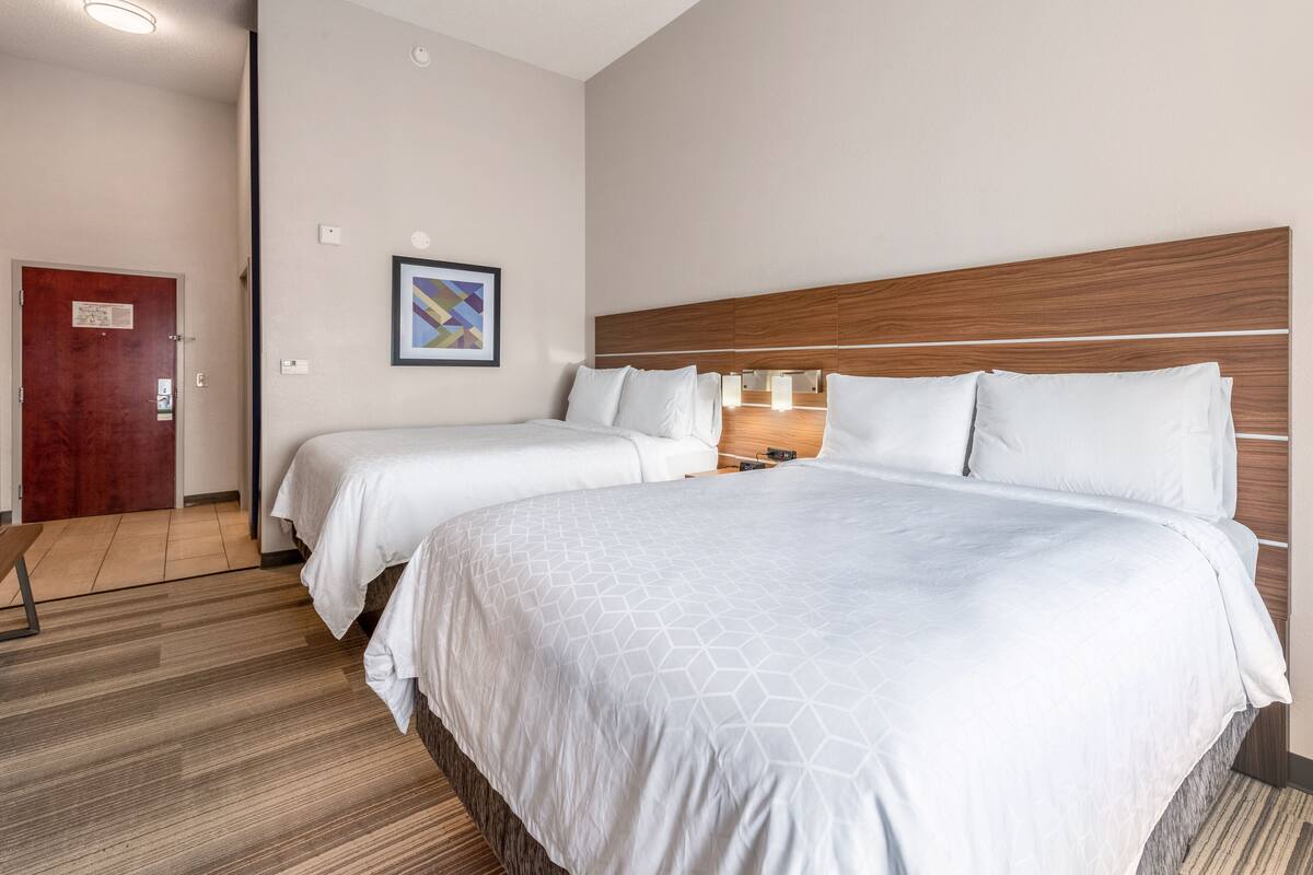 A hotel room with two beds, a wooden headboard, a framed picture on the wall, and a wooden floor.