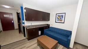A compact living space with a kitchenette, a blue sofa, and a wooden coffee table.