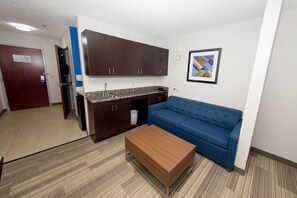 A compact living space with a kitchenette, a blue sofa, and a wooden coffee table.