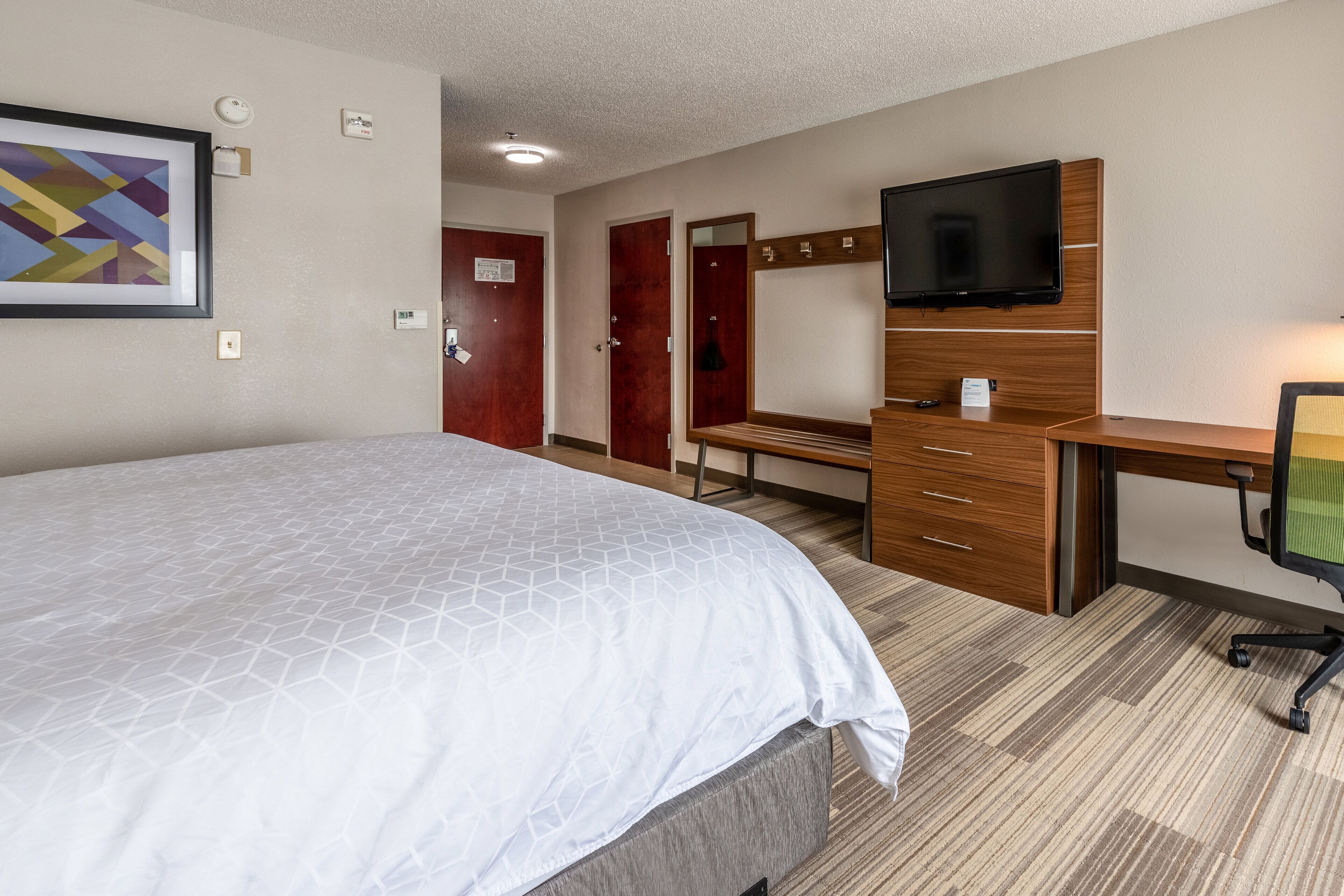 A hotel room with a large bed, a wooden desk, a television, and a framed picture on the wall.