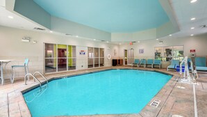 An indoor swimming pool with clear water, a lifeguard chair, and a shallow water sign.