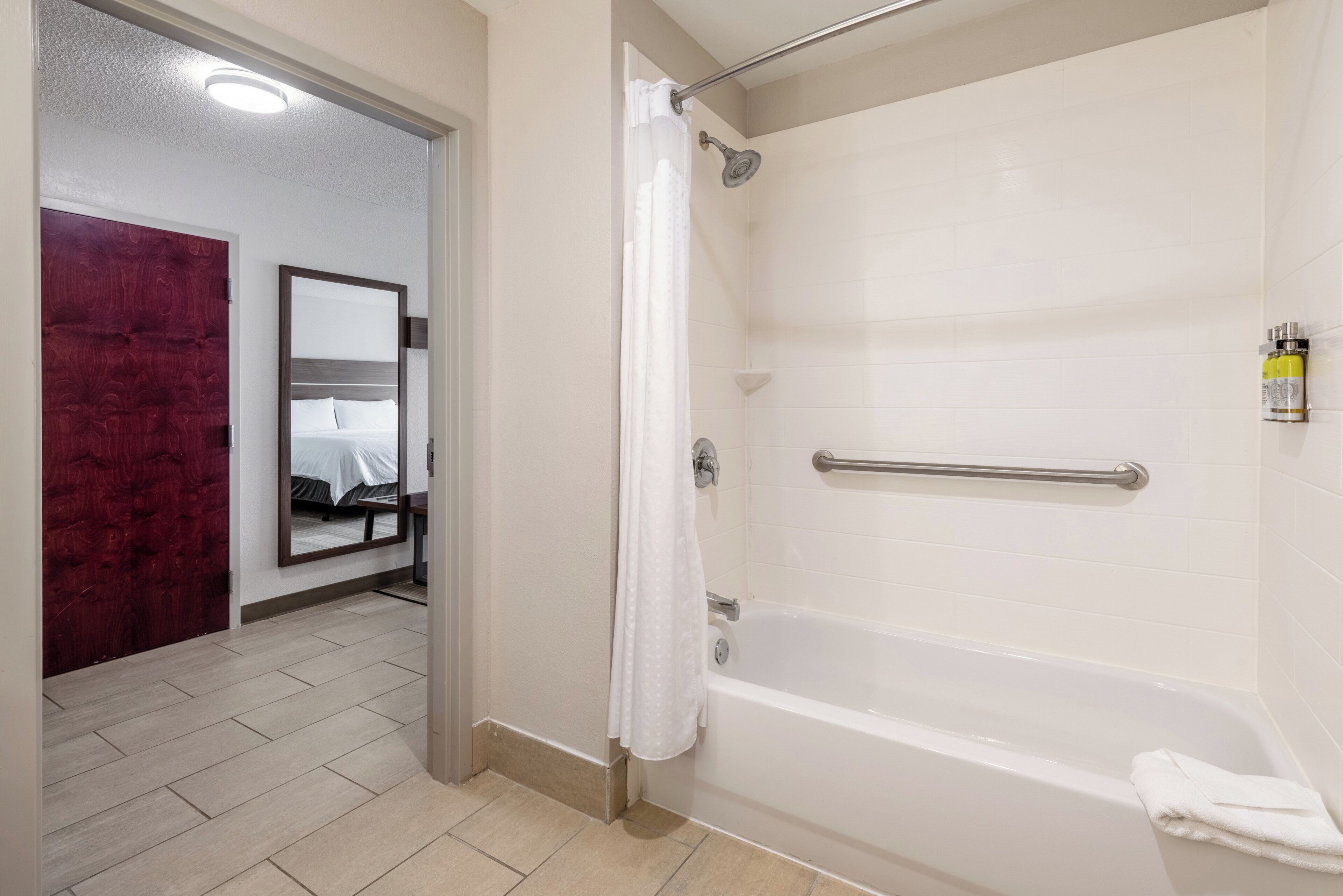 A bathroom with a white bathtub, a shower curtain, a handrail, and a towel.