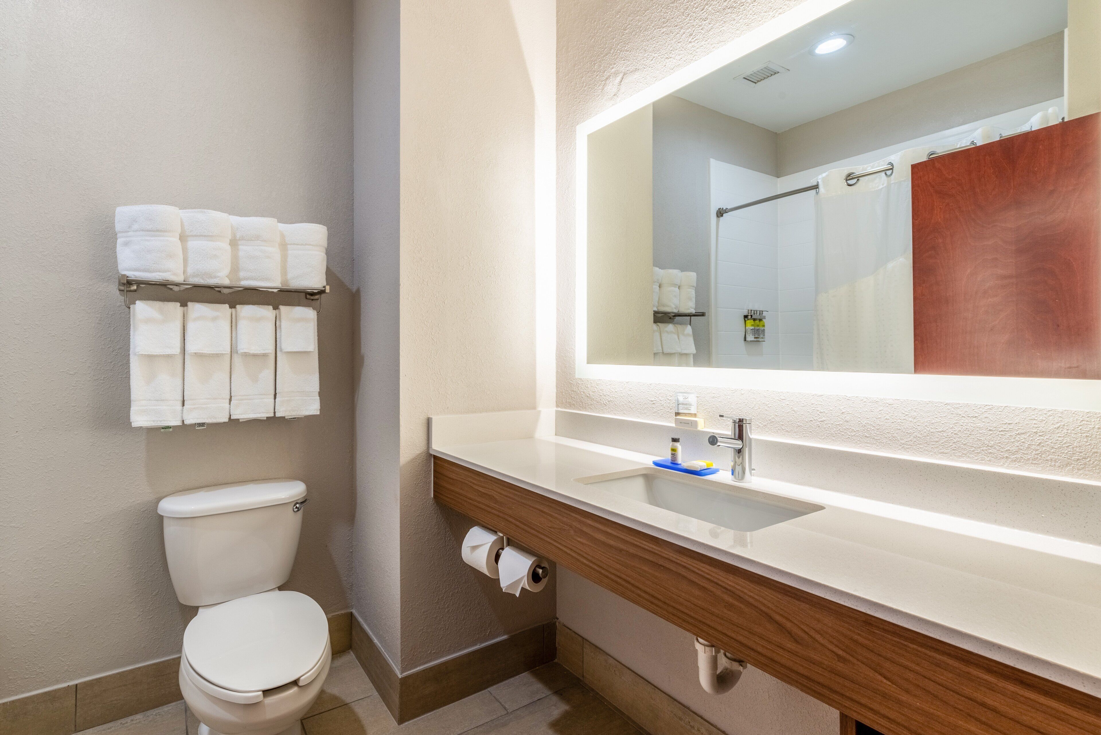 A modern bathroom with a toilet, a sink with a mirror, and a towel rack with multiple towels.