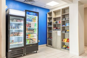Un distributeur automatique rempli d’en-cas et de boissons, situé à côté d’une étagère en bois dotée de paniers de rangement.