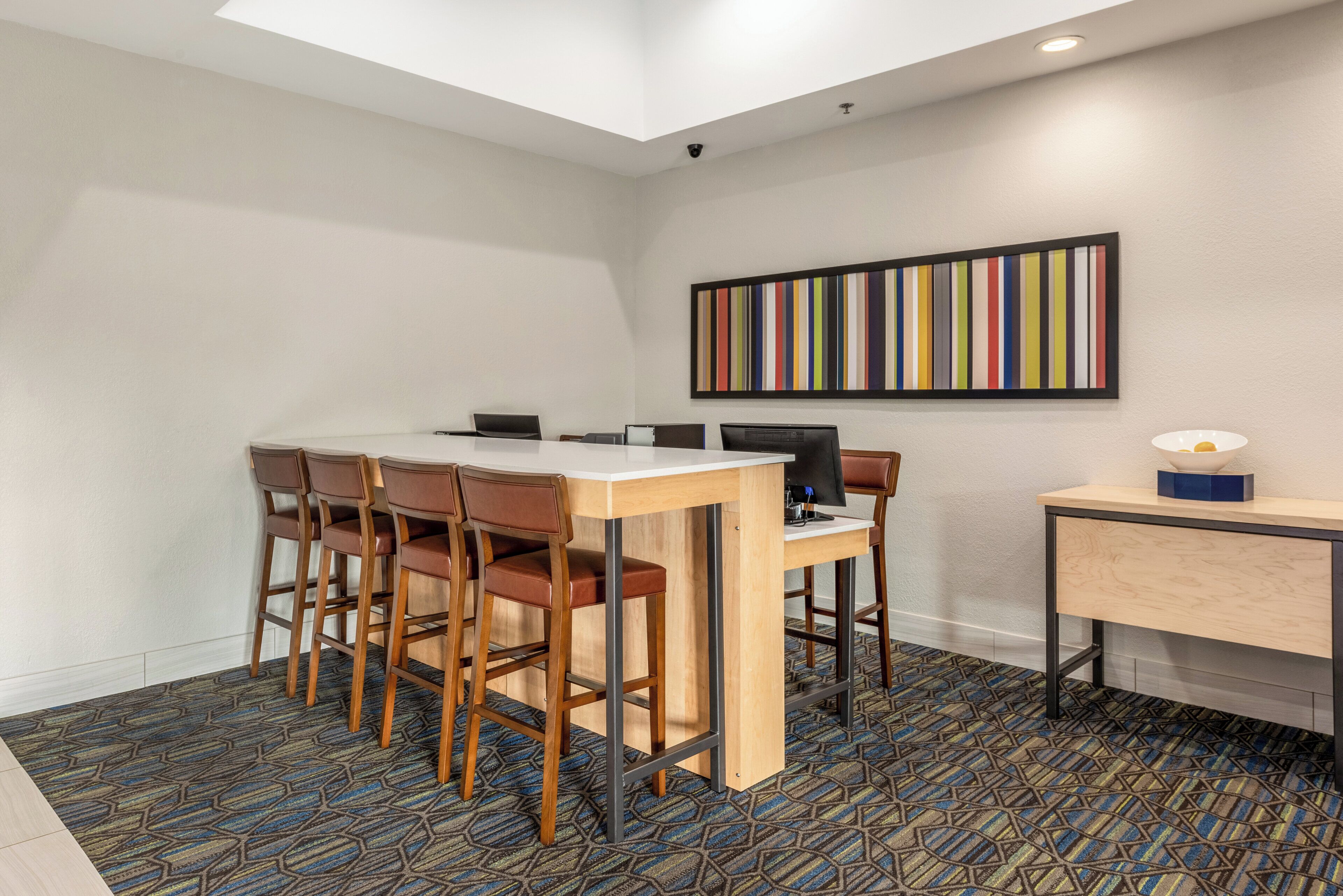 A conference room with a table, chairs, computers, and a desk with a lamp.