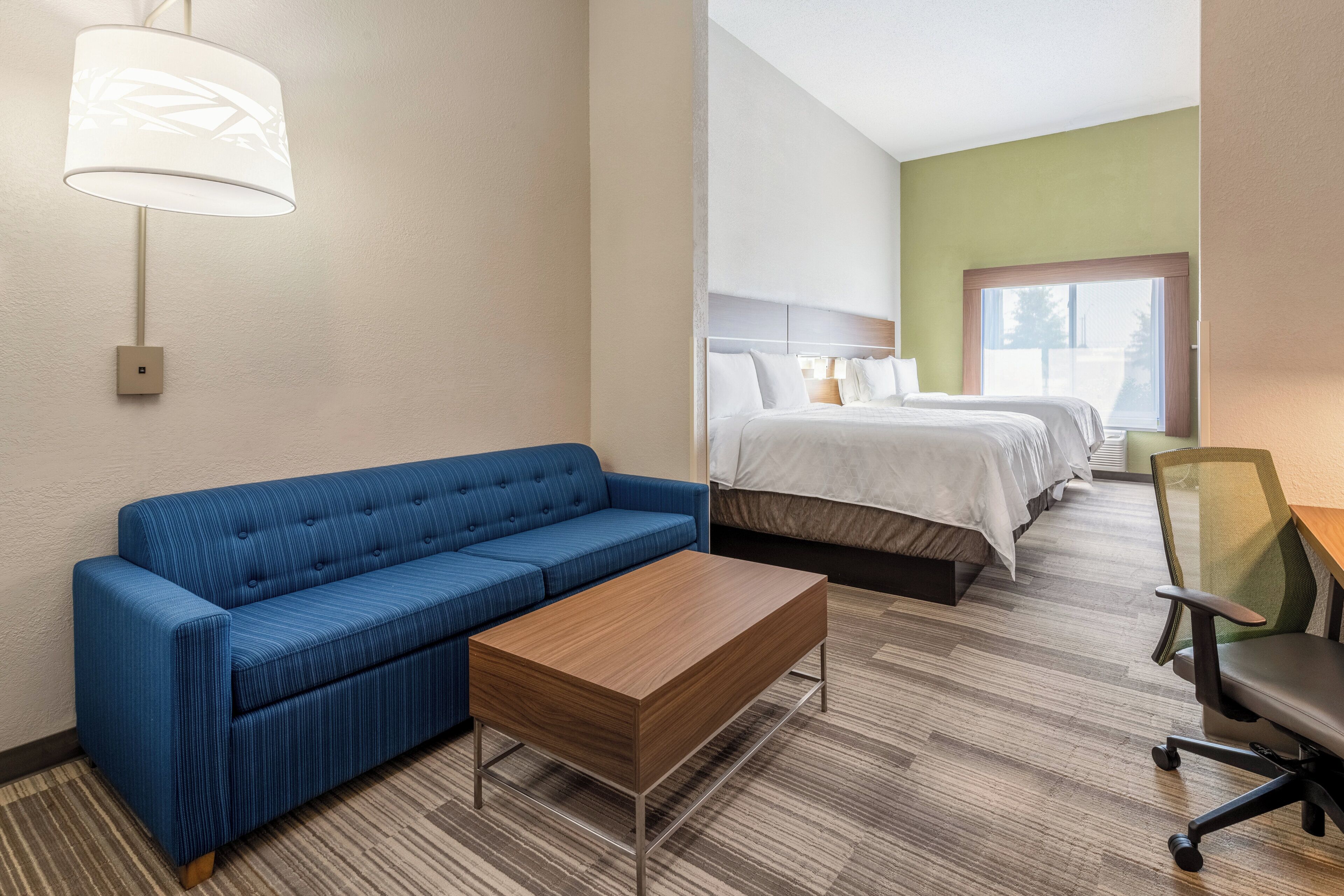 A hotel room with a blue sofa, a wooden coffee table, a single bed, a double bed, and a chair.