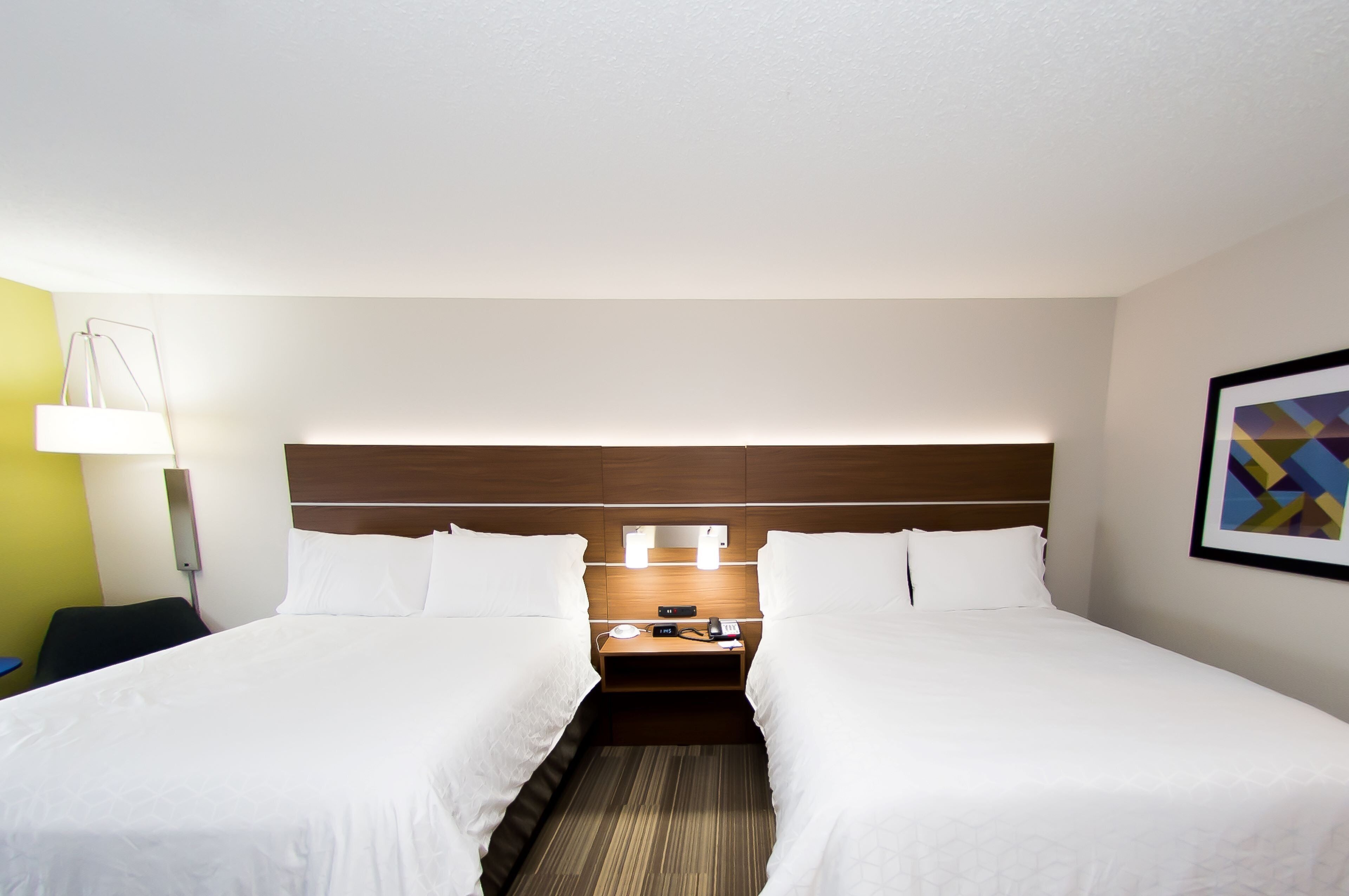 Habitación de hotel con dos camas, una mesita de noche con lámpara y un teléfono en la pared.
