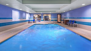 An indoor swimming pool with blue and beige tiled walls, a reception area with a counter and chairs, and a view into the adjacent room. - Holiday Inn Express Picayune-Stennis Space Center by IHG (Picayune)
