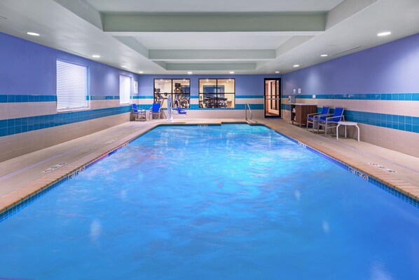 An indoor swimming pool with blue and beige tiled walls, a reception area with a counter and chairs, and a view into the adjacent room. - Holiday Inn Express Picayune-Stennis Space Center by IHG (Picayune)