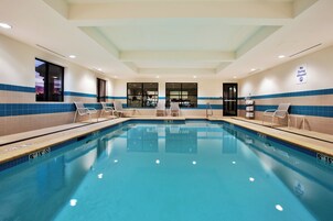 Una amplia piscina interior con agua cristalina, rodeada de sillas de descanso y vistas a equipo de ejercicio al fondo.