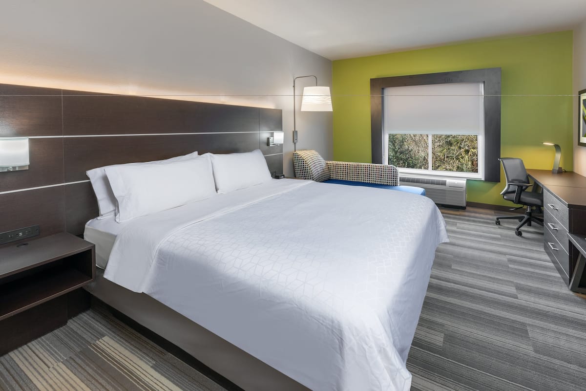 A modern hotel room with a large bed, a desk, and a chair.