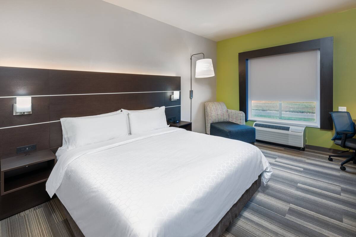 A hotel room with a large bed, a desk with a lamp, a chair, and a window with a view.