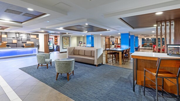 A modern hotel lobby with a reception desk, seating area, and a dining space. - Holiday Inn Express Picayune-Stennis Space Center by IHG (Picayune)
