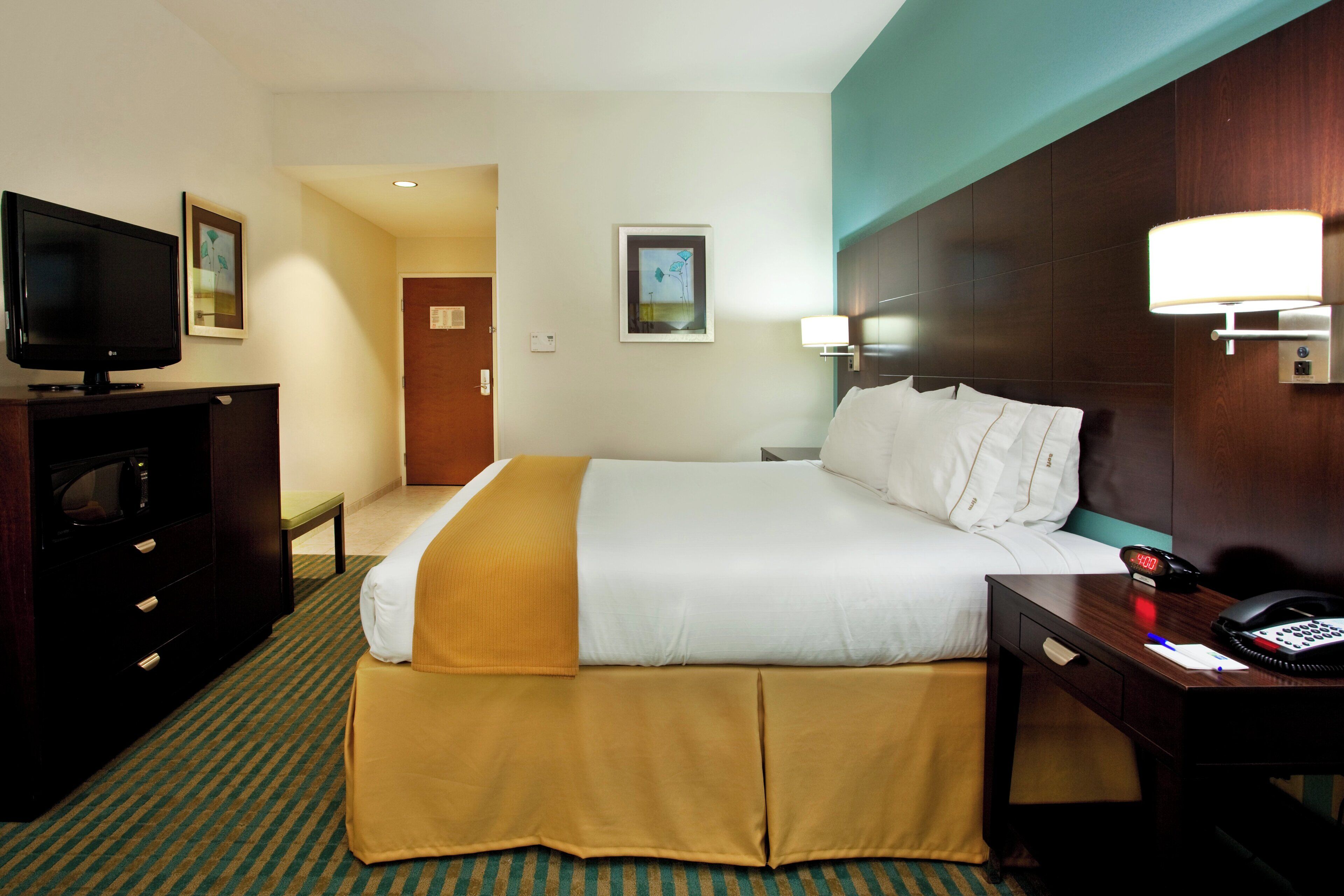 A hotel room with a bed, a desk with a telephone, a television, and a microwave.