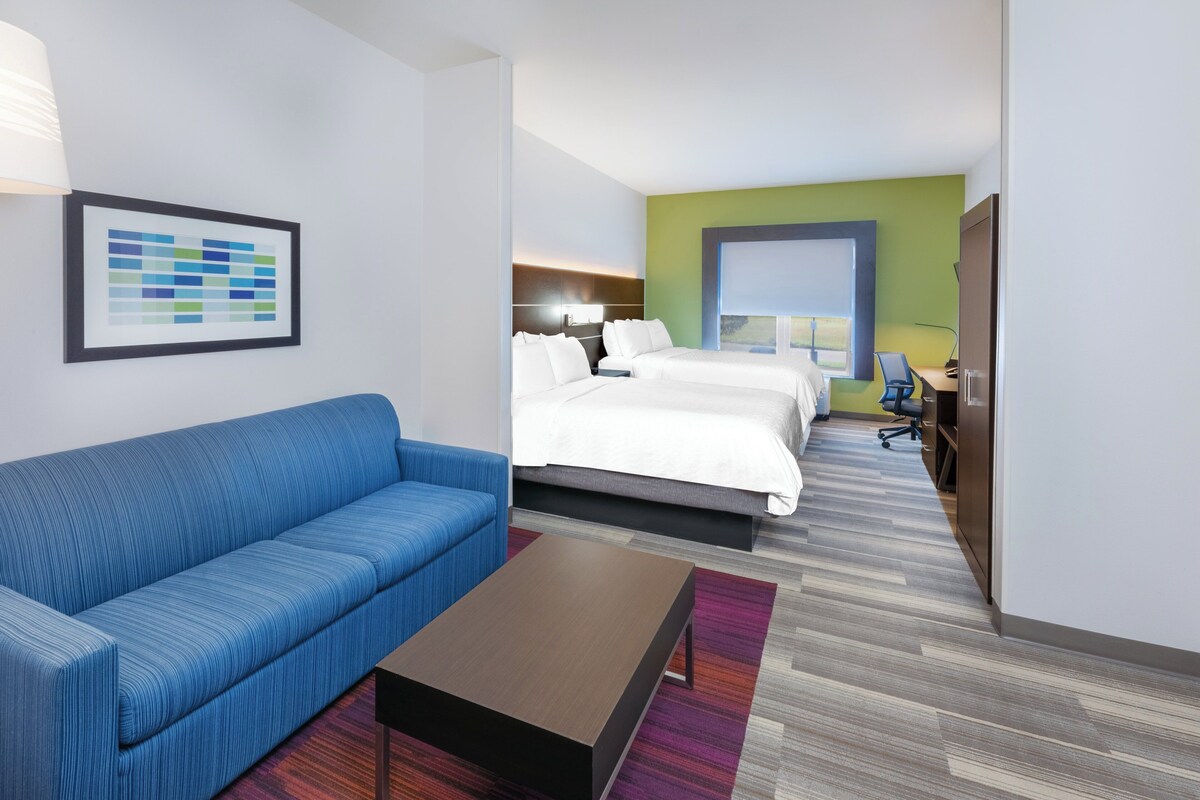 A hotel room with a blue sofa, a bed with white bedding, a desk with a chair, and a framed picture on the wall.