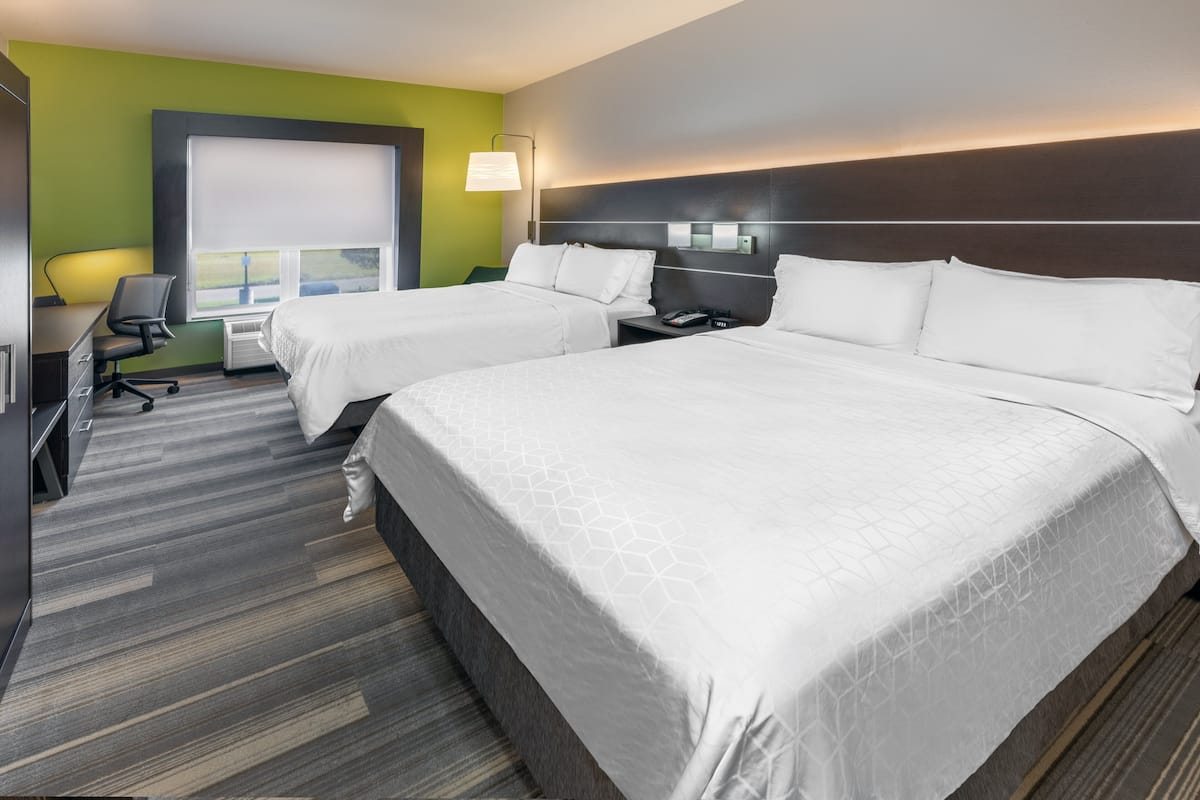 A hotel room with two beds, a desk, a chair, and a large window.