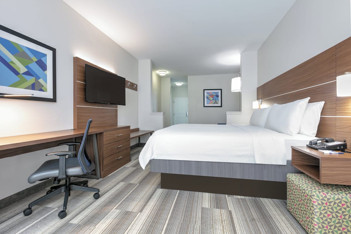 A hotel room with a large bed, a desk with a chair, a television, and a small table with a lamp.