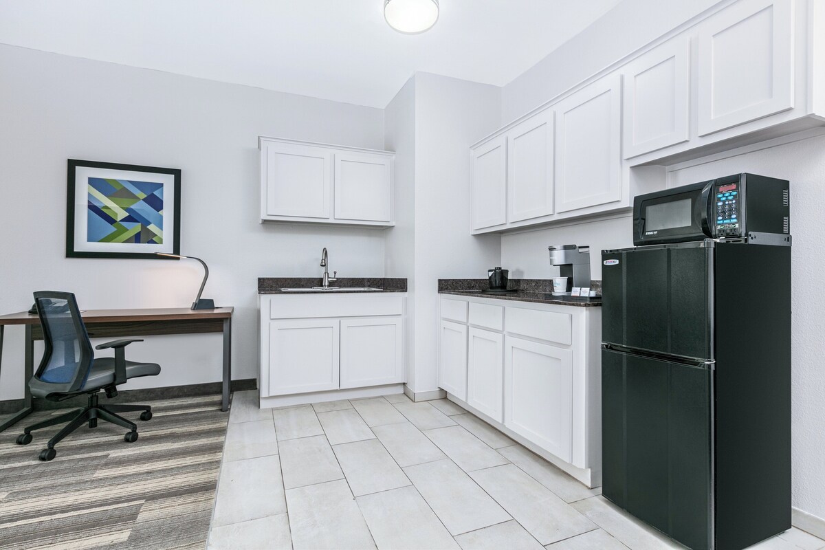A modern kitchen with white cabinets, a black refrigerator, a microwave, and a coffee maker.