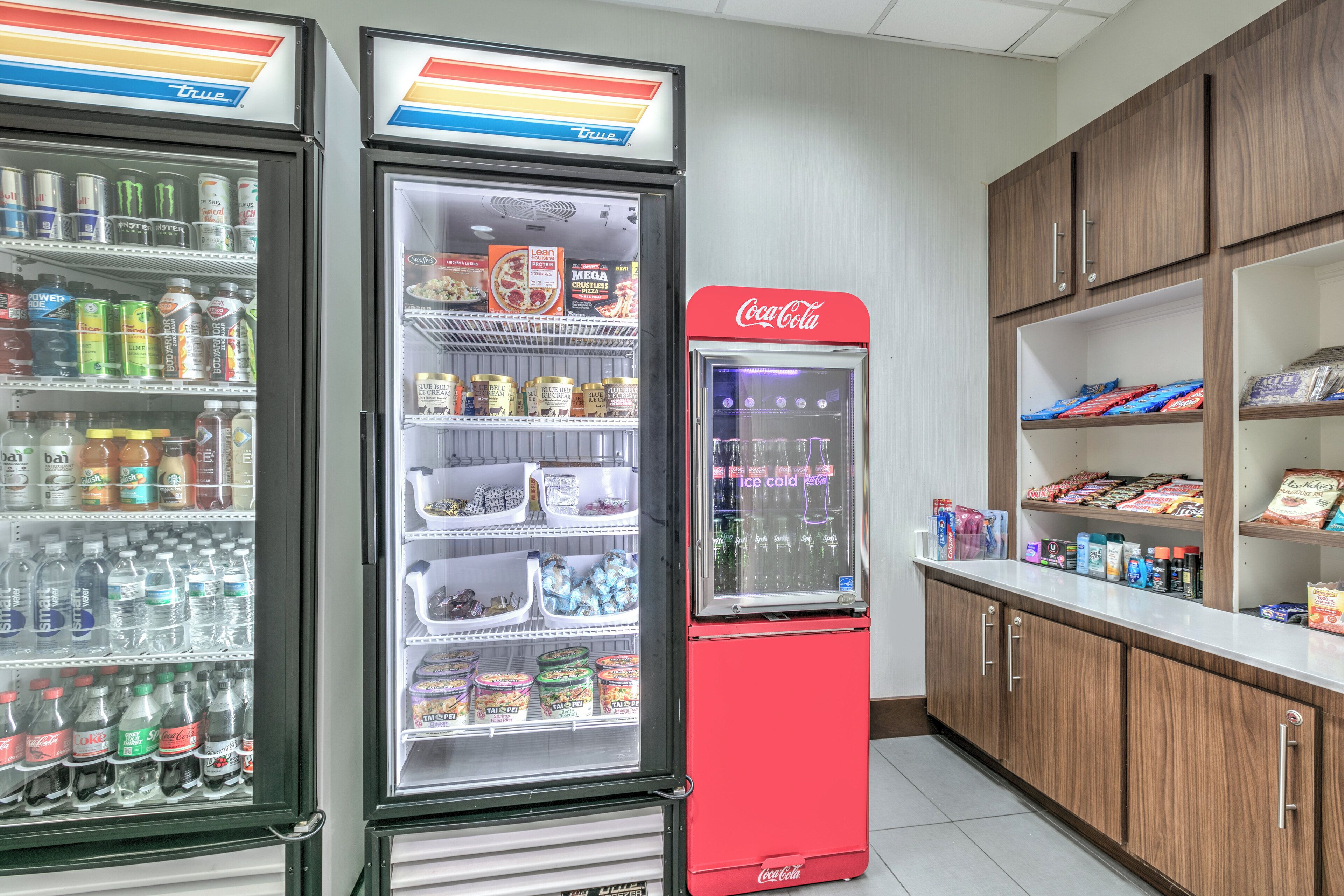 Een automaatruimte met een Coca-Cola koeler en twee andere drankautomaten, gevuld met verschillende dranken en snacks.