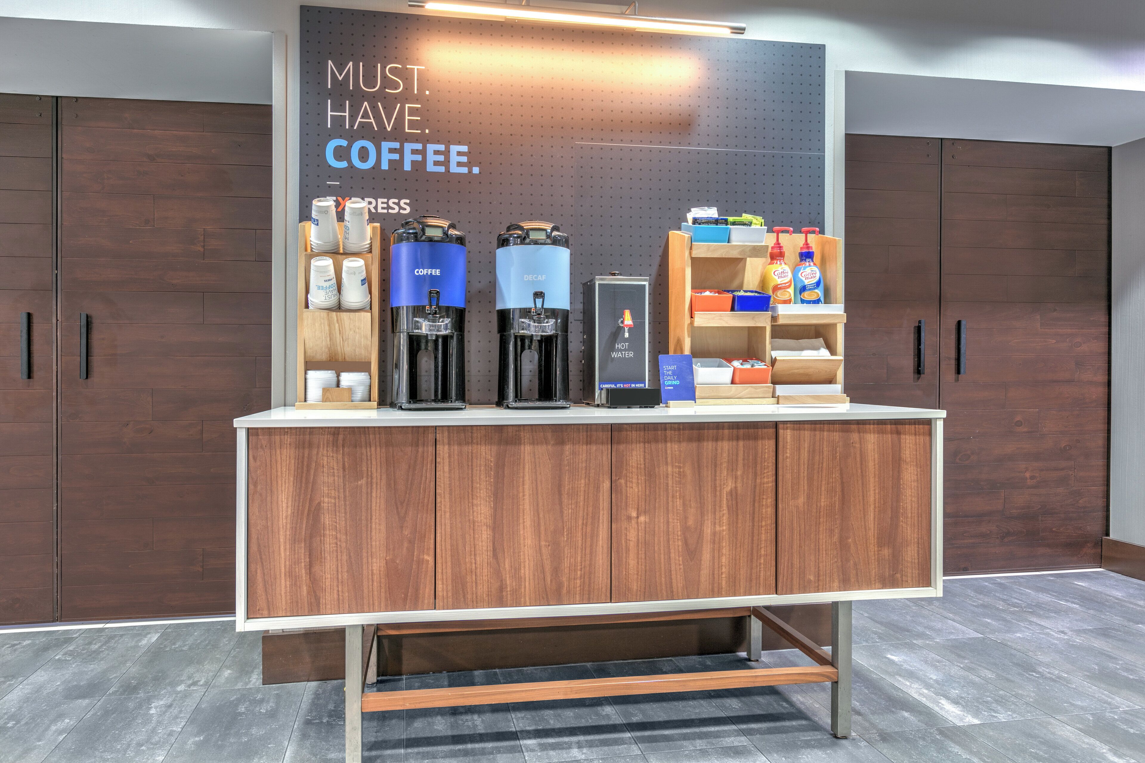 A modern coffee station with espresso machines, a hot water dispenser, and a variety of coffee products.