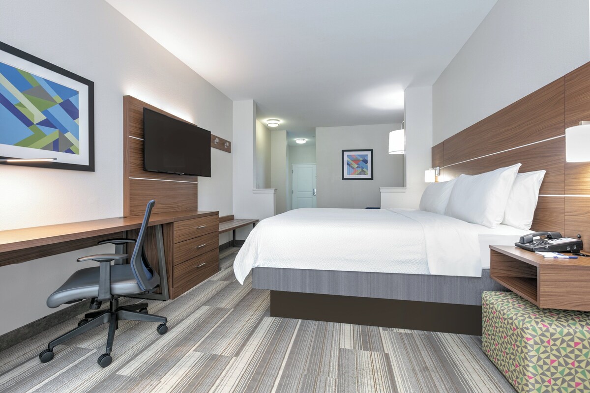 A hotel room with a large bed, a desk with a chair, a television, and a small table with a lamp.