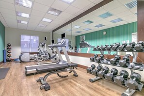 A gym with cardio machines, weight benches, and dumbbells.