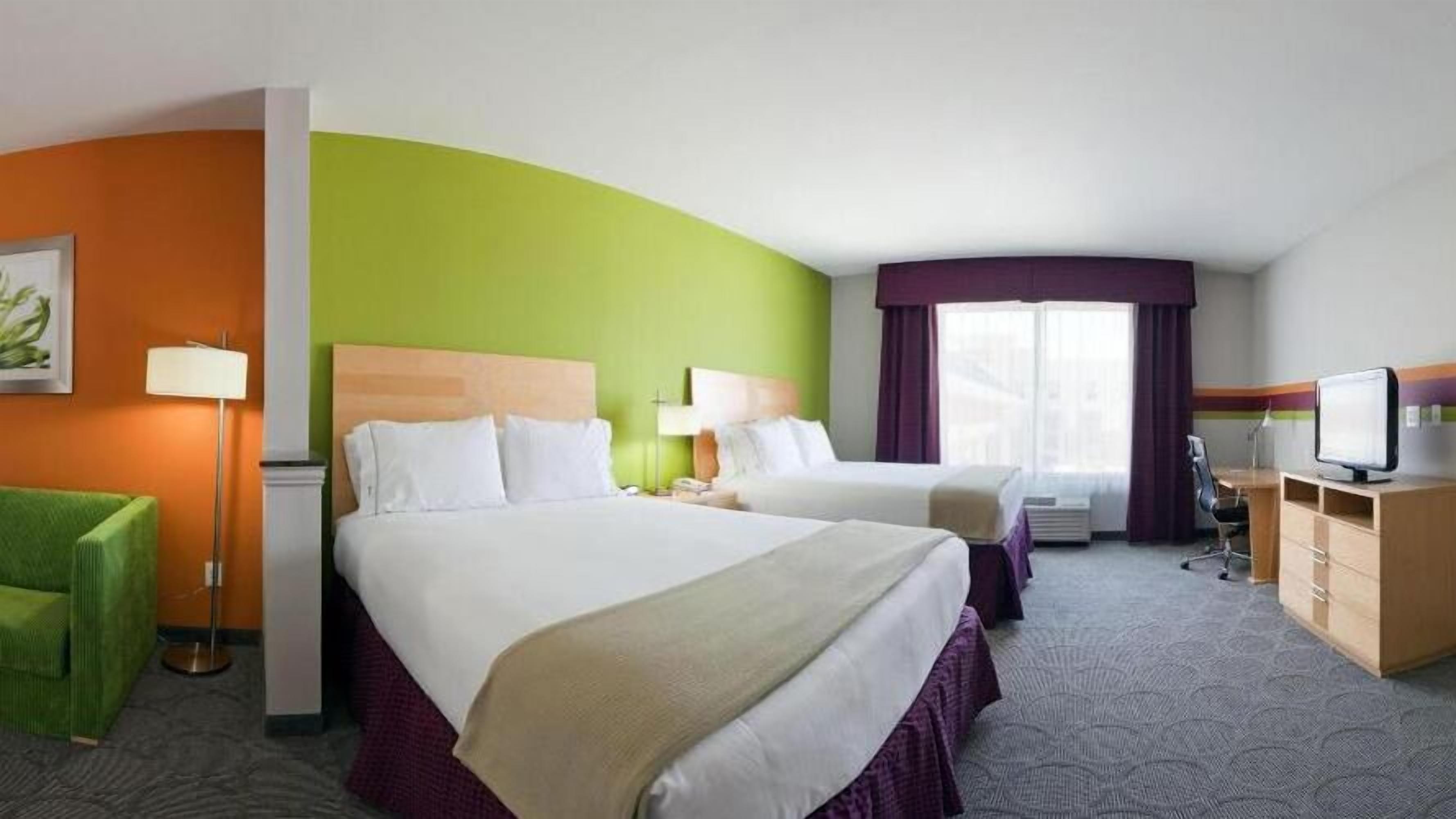 A hotel room with two beds, a desk, a chair, a TV, and a lamp.