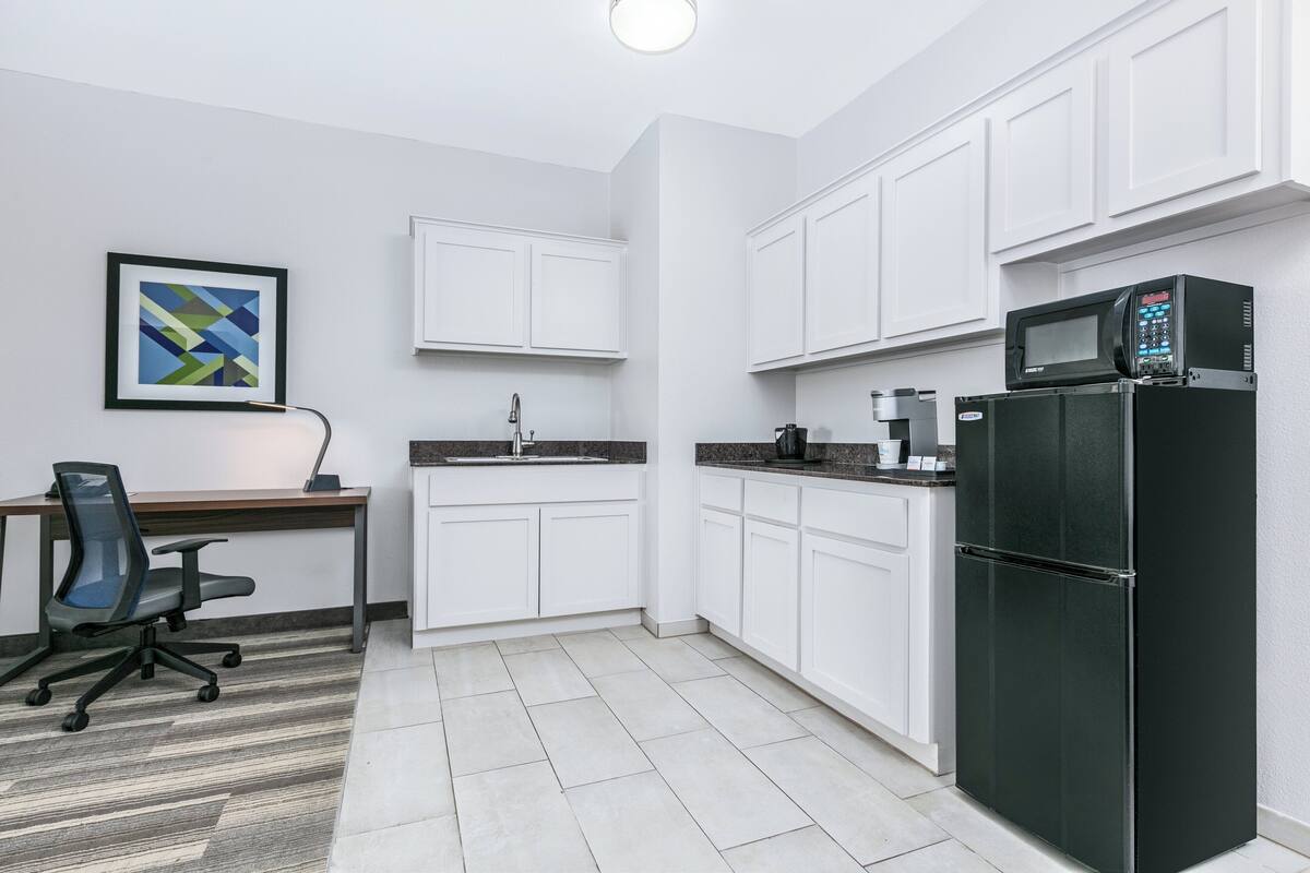 A modern kitchen with white cabinets, a black refrigerator, a microwave, and a coffee maker.