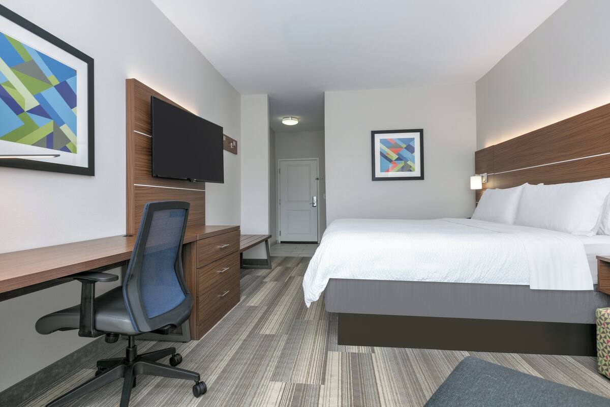 A modern hotel room with a bed, desk, chair, and a flat-screen TV mounted on the wall.