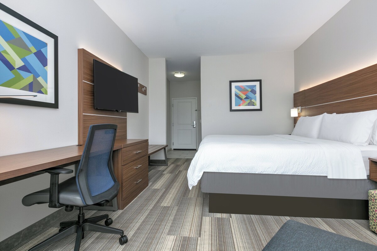 A modern hotel room with a bed, desk, chair, and a flat-screen TV mounted on the wall.