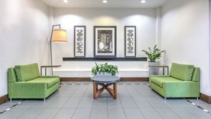 Un hall con dos sofás verdes, una mesa redonda, una lámpara de pie y obras de arte enmarcadas en la pared.