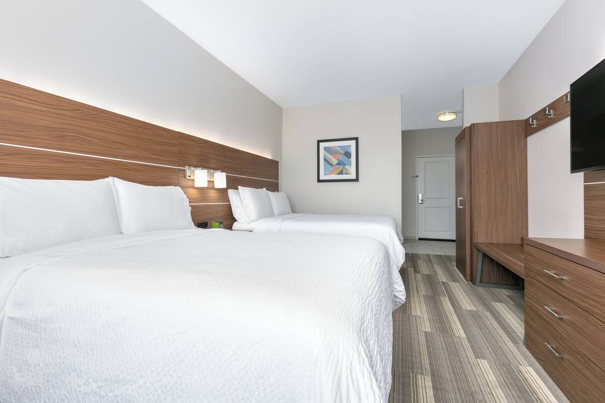 A hotel room with two beds, wooden headboard, a flat-screen TV, and a framed picture on the wall.