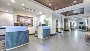 Un moderno vestíbulo de hotel con dos mostradores de recepción, una gran pantalla digital y un diseño espacioso con plantas en macetas.