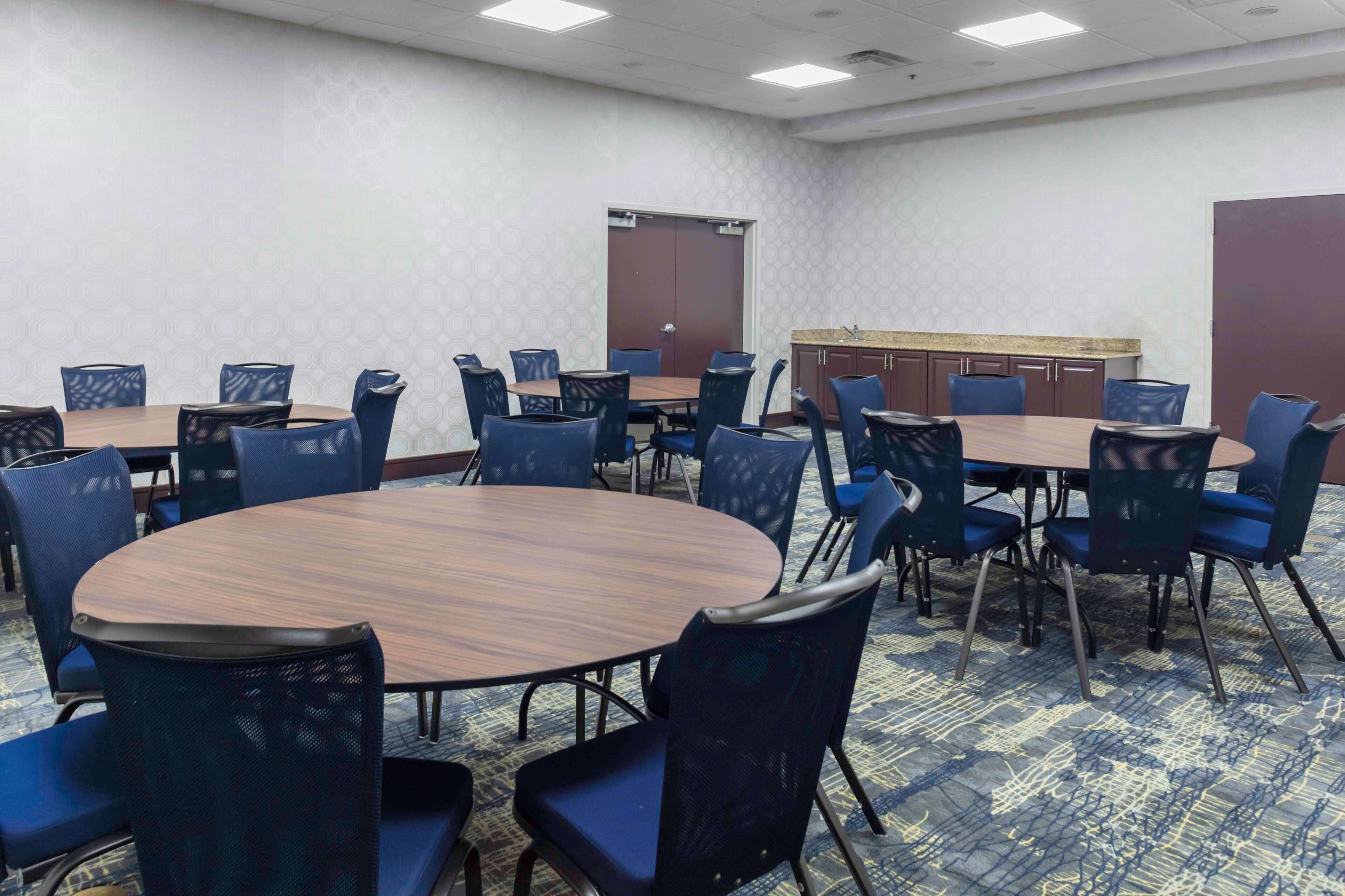A conference room with round tables and blue chairs, carpeted floor, and a door in the background.