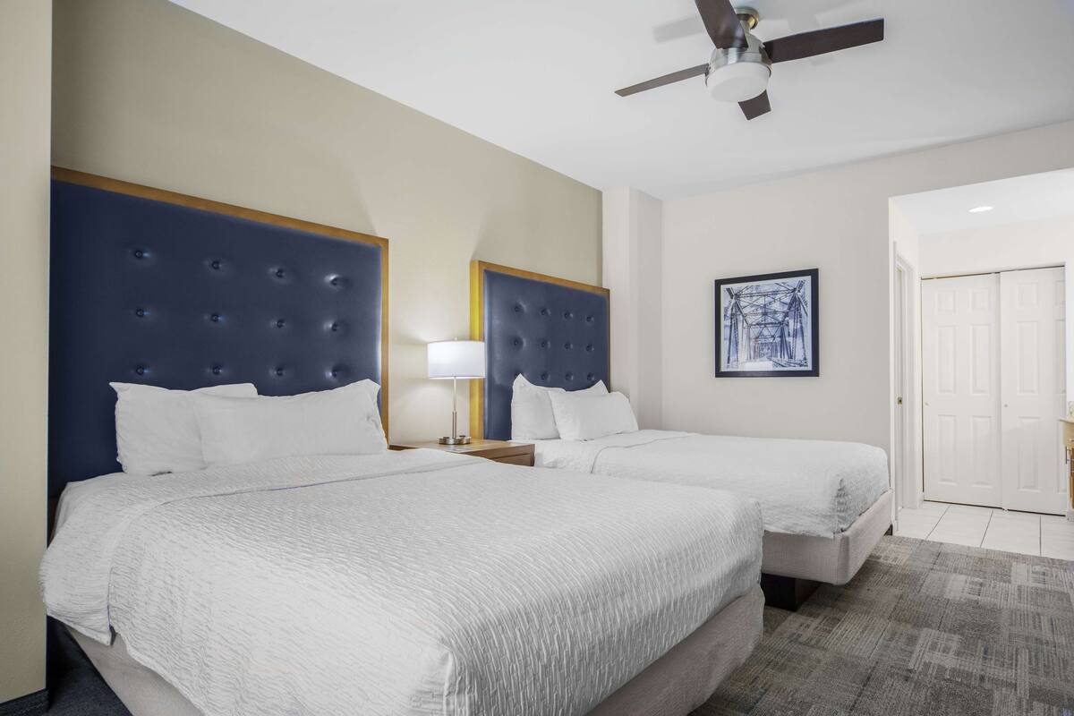 A hotel room with two beds, a ceiling fan, a framed picture on the wall, and a door.