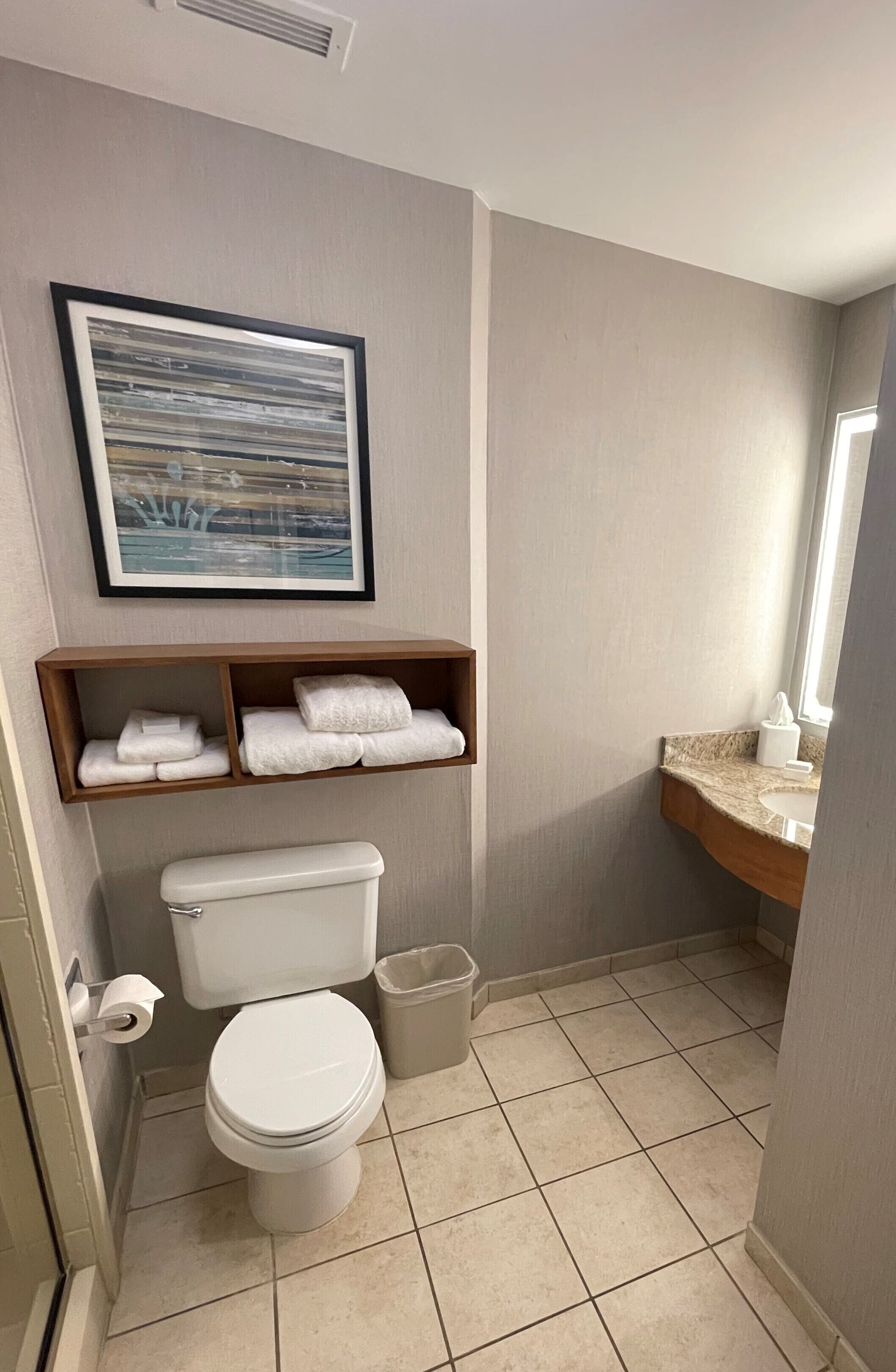 Une petite salle de bain comprenant des toilettes, un lavabo, un tableau encadré et une étagère avec des serviettes.