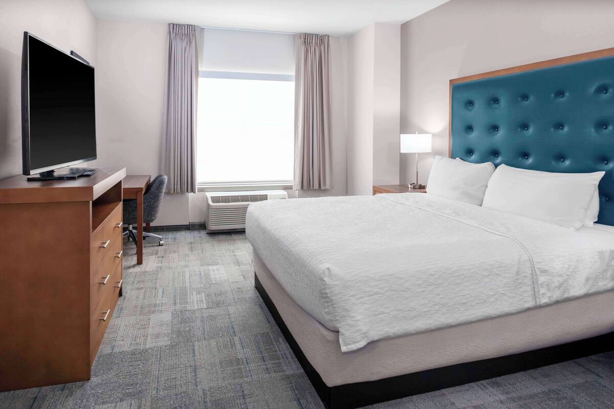 A hotel room with a large bed, a flat-screen TV, a desk with a chair, and a window with curtains.