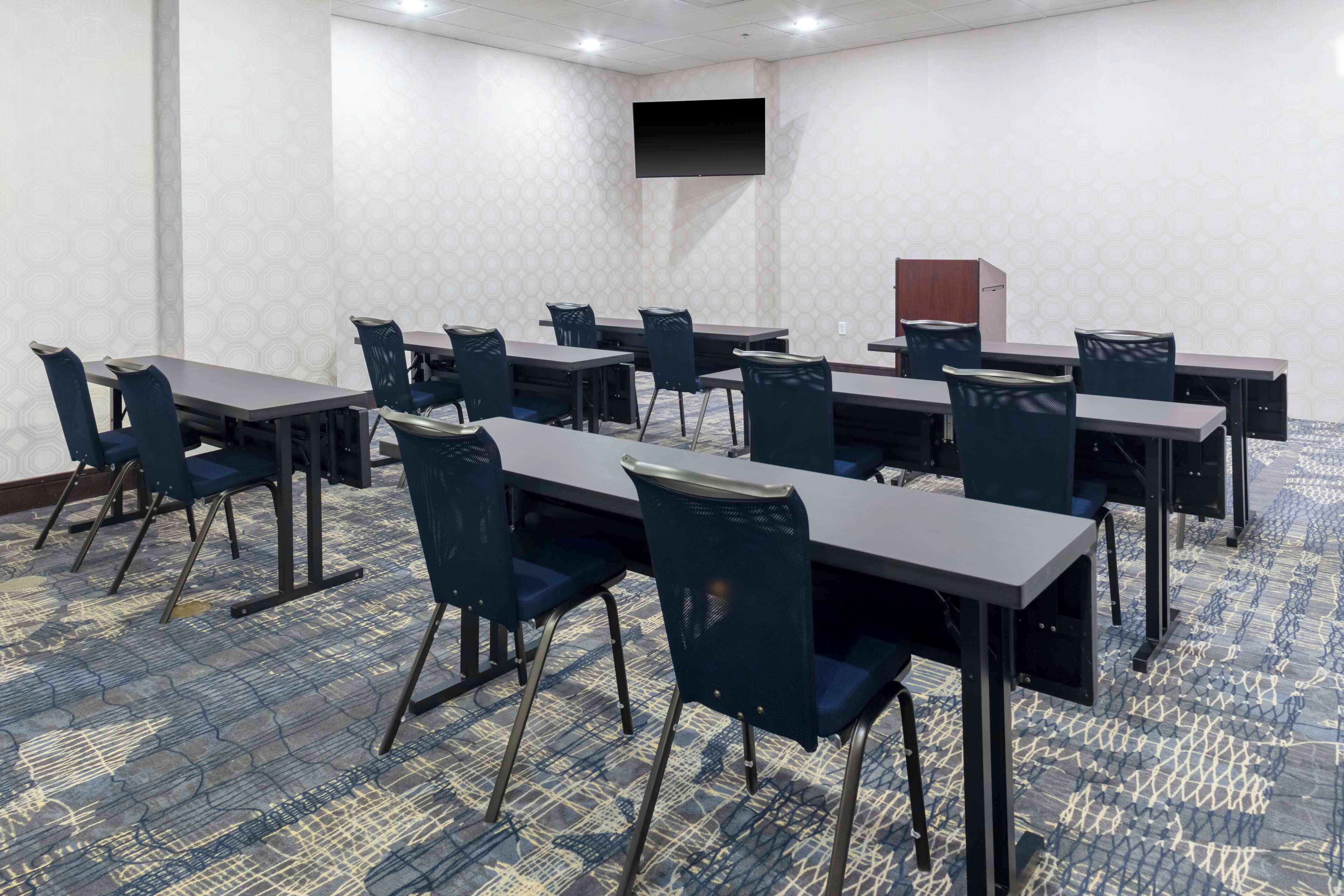 Una sala de conferencias con mesas y sillas, un televisor de pantalla plana y una alfombra estampada.