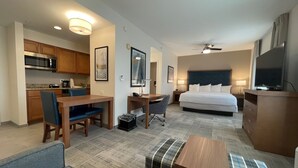 Habitación de hotel con cama, escritorio, silla, kitchenette y televisor.