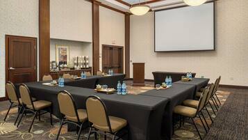 Una sala de conferencias con una mesa larga, sillas, botellas de agua y una pantalla de proyector.