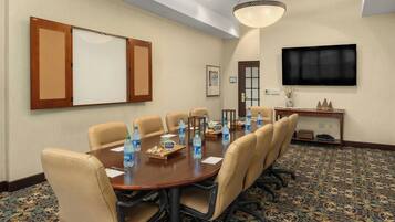 A conference room with a long table, beige chairs, water bottles, and a TV on the wall.