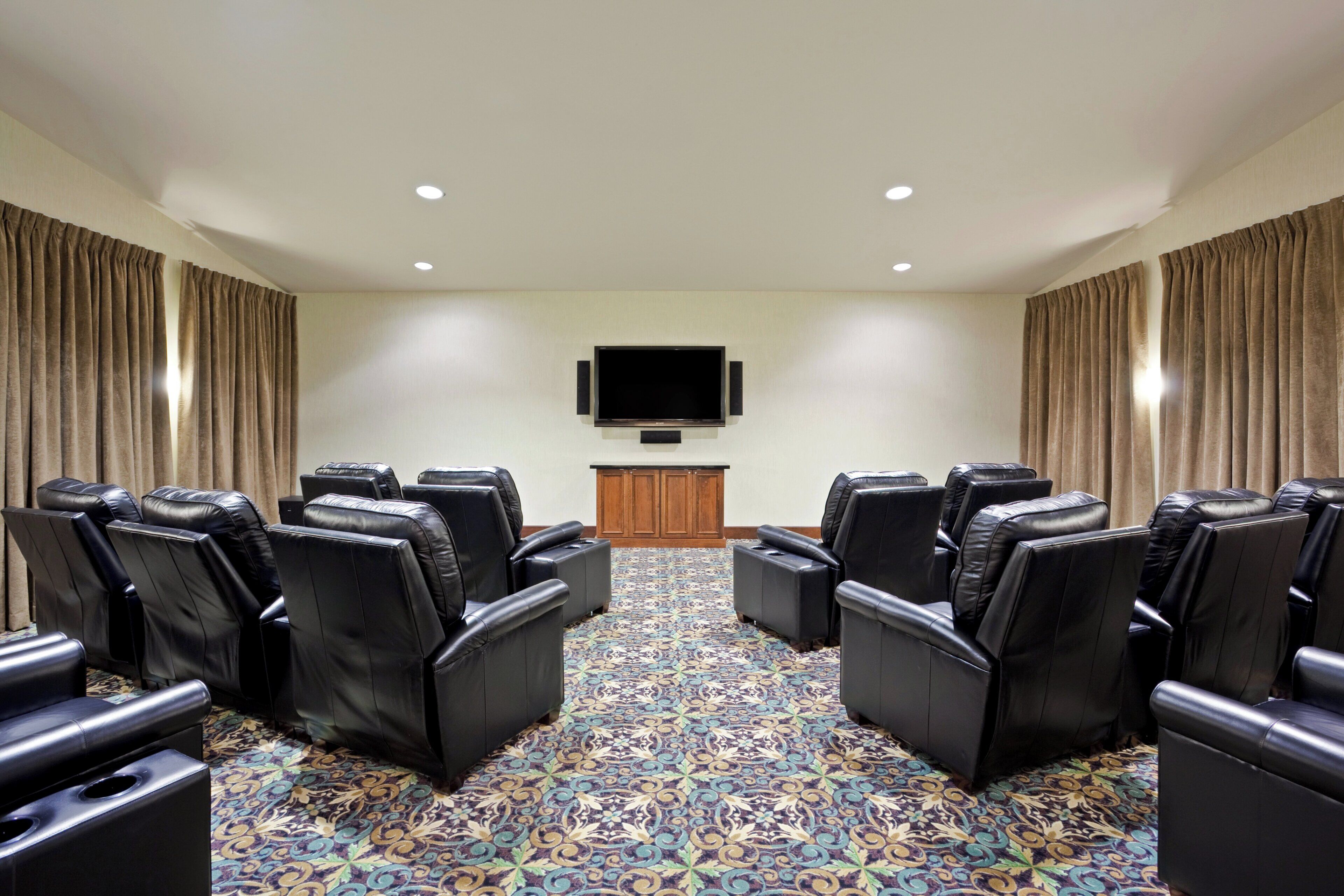 A room with black leather reclining chairs arranged in a semi-circle facing a flat-screen TV mounted on the wall.
